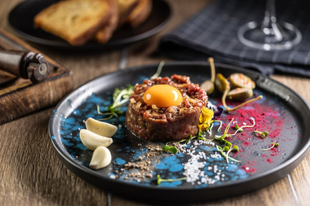 Beef tartare with egg yolk on a plate with garlic and toasted bread.の写真素材