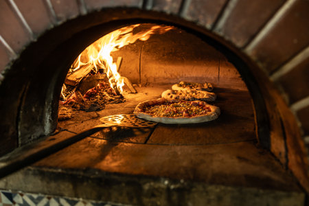 Traditional oven for baking pizza with burning wood and shovel. The cook rotates the pizza in the oven to ensure even baking.の写真素材