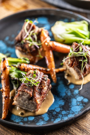 Three pieces of baked belly with grilled vegetables on a plate in a pub or restaurant.の写真素材