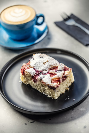 Fruity plum cake on a plate and next to a mug with coffee on a table in a cafe.の写真素材