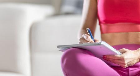 Sporty woman sits on a mat and writes down future training plans for achieving sports results.