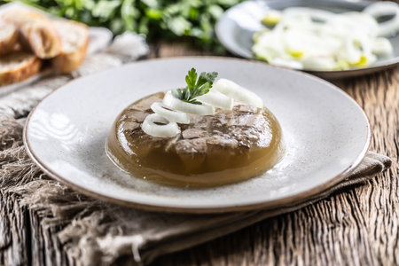 Homemade pork aspic, meat jelly with onion and leek in a white plate.