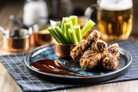 Fried chicken legs with celery sticks and draft beer on plate in pub or restaurant.の写真素材