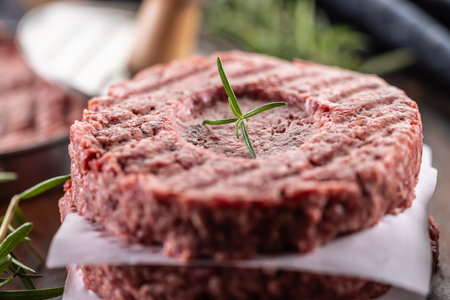 Fresh raw ground beef patties with rosemary salt and pepper made in a meat form on a cutting board.の写真素材