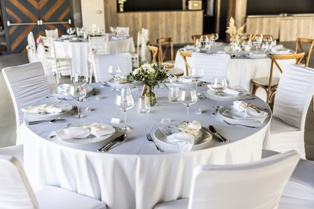 A wedding table covered with a white tablecloth, decorated with flowers, candles, glasses and cutlery.の写真素材