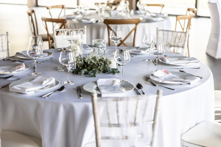 A wedding table covered with a white tablecloth, decorated with flowers, candles, glasses and cutlery.の写真素材