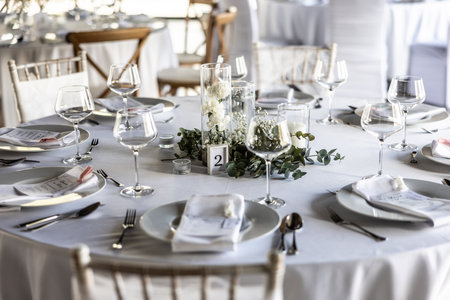 A wedding table covered with a white tablecloth, decorated with flowers, candles, glasses and cutlery.の写真素材