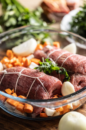 Raw beef tenderloin in a glass baking dish with root vegetables, ready to be processed into the Czech national dish - Sirloin on cream.の写真素材