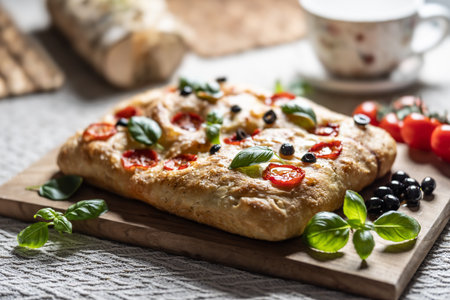 Focaccia - Italian Bread with tomatoes basil leaves olives and olive oil on cutting board.