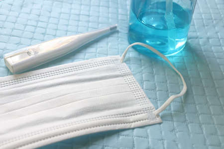 Closeup mercury, white mask and blue alcohol gel bottle on blue plastic background, side view,...