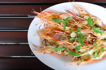 Top view, close up grilled fresh river shrimp with seafood sauce, slice garlic and mint leaves in white plate on wood table background is famous food in Thailand look delicious. Have copyspace.の写真素材
