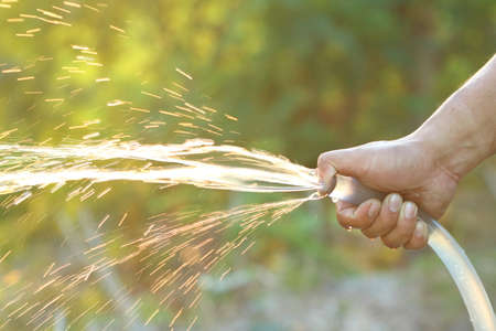 People hand use fingure close watering end of rubber water hose then water like spray with sunlight for agriculture feed tree, can use for World for Water Dayの写真素材