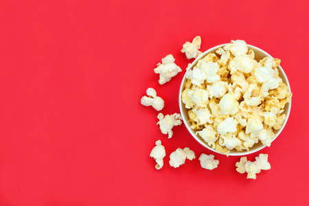 Top view isolated salted popcorn mix with cheese popcorn spilled from white bowl on red table...