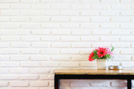 Fake pink and red flower bouquet in white vase on wood table on white brick wall texture background have copy space for put text. Beautiful view of home interior.の写真素材