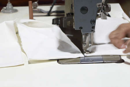 Closeup hand of Asian woman sew white fabric by industrial sewing machine
