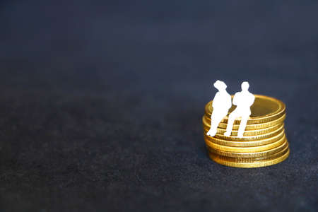 couple white miniature business people sitting on golden coins pile, on black background have copy space for put text, concept growing golden coins for businessの写真素材