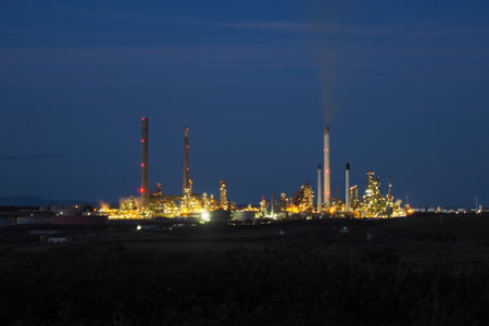 Pembroke oil refinery lit up at night with smoke rising from a chimney stack, Rhoscrowther on the...