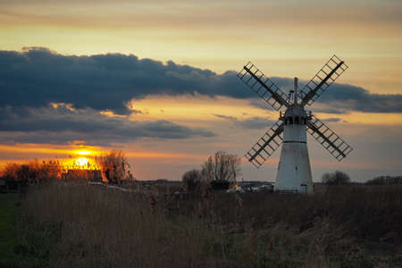 Beautiful orange sunset lighting up the clouds over Thurne Dyke Drainage Mill set in The Broads,...