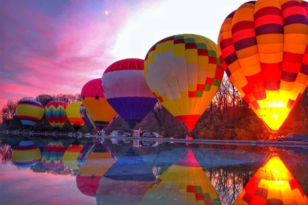 A row of hot air balloons light up next to a reflecting pool at a local festivalの素材