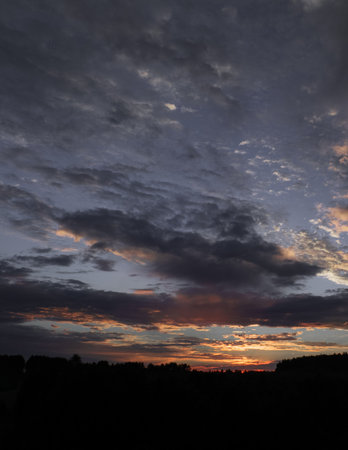 A breathtaking sunset with textured clouds drifting across the sky. The warm hues of the setting sun contrast beautifully with the deepening twilight tones, creating a moody and atmospheric scene.の写真素材