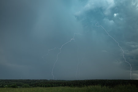 Sharp lightning bolts cut across a darkening sky during a summer thunderstorm, electrifying the...