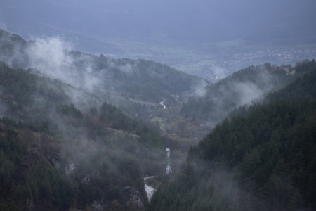 A peaceful valley stretches between forest-covered hills, a narrow stream weaving its way through...