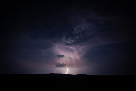 A striking photograph of a nighttime thunderstorm, featuring a powerful lightning bolt illuminating...