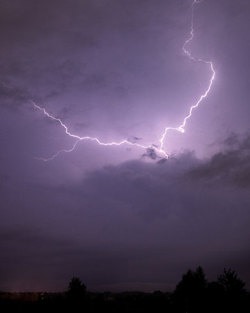 A jagged bolt of lightning tears across a dramatic purple thunderstorm sky, illuminating the night...