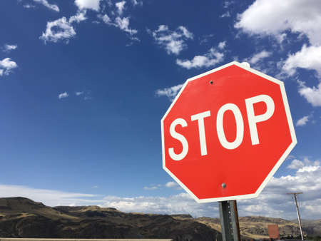Red Stop traffic sign for safety driving with big blue sky,clouds and mountainの素材