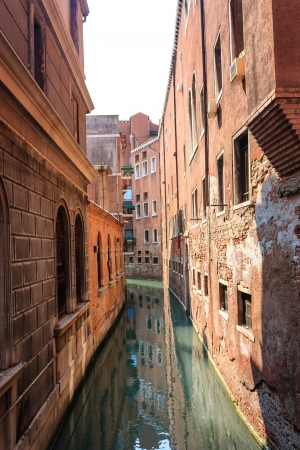 Buildings reflect on the surface of a small narrow canal in the city of Veniceの写真素材