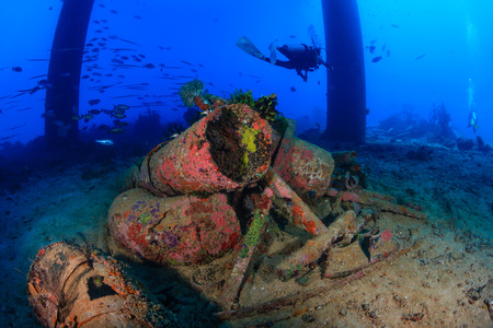 SCUBA divers swim past underwater pipes and other wreckage underneath an oil rigの写真素材