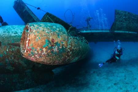 SCUBA diver swimming next to the jet engine attached to the wreckage of a sunken aircraftの写真素材
