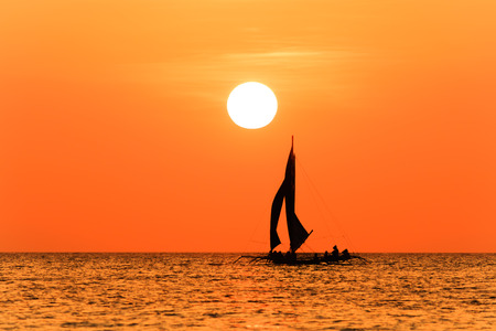 Traditional sailing boat and a tropical sunset on a calm oceanの写真素材