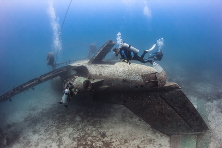 SCUBA divers exploring the upturned fuselage of an underwater aircraft wreckの写真素材