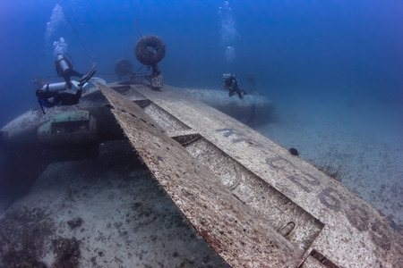 SCUBA divers over the wing of an upside down aircraft wreck on the seabedの写真素材