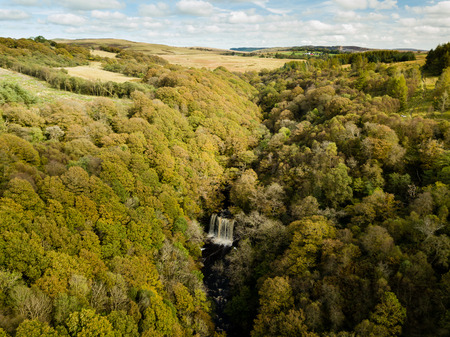 Aerial view of a large waterfall in a tree lined valley during autumnの写真素材