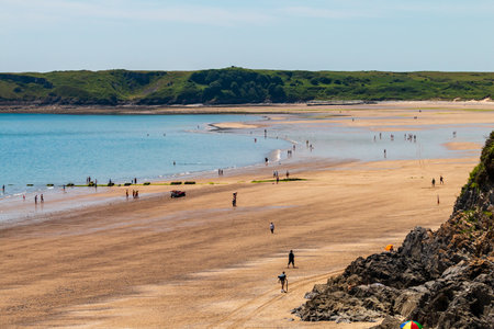 Tourists on a huge, wide sandy beach and shallow ocean on a sunny, summers day (Tenby, Wales)のeditorial素材