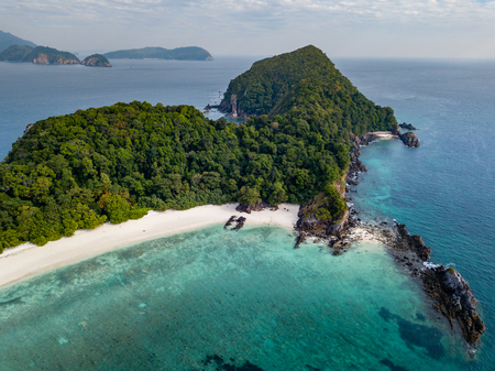 Aerial drone view of a beautiful tropical island containing a deserted sandy beach and lush green...