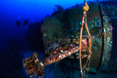 SCUBA divers exploring a deep, underwater shipwreck in a clear, tropical oceanの写真素材