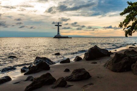 Sunset behind a large cross marking an old, sunken cemetery under the tropical ocean (Camiguin, Philippines)の写真素材