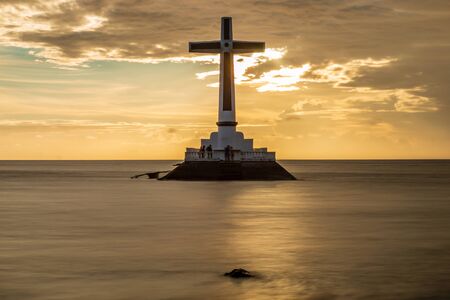 Sunset behind a large cross marking an old, sunken cemetery under the tropical ocean (Camiguin, Philippines)の写真素材