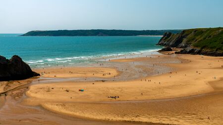 Waves breaking onto a large sandy beach with surrounding cliffsの写真素材