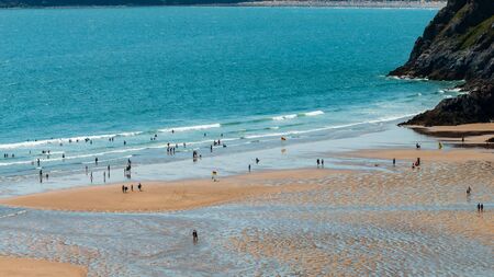 THREE CLIFFS BAY, WALES - Swimmers and sunbathers enjoy a warm, sunny day at Three Cliffs Bay on the Gower Peninsula in Walesの写真素材