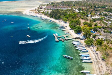Aerial view of boats moored off a beautiful tropical coral reef and beach on a small island (Gili...