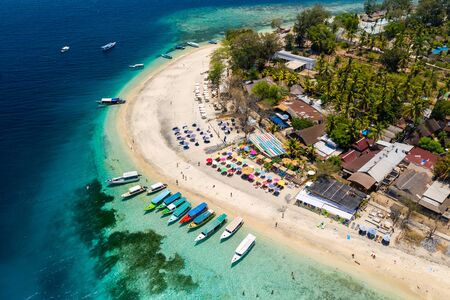 Top down aerial view of colorful boats and sunshades on a tropical beach on a small island fringed by a coral reefの写真素材