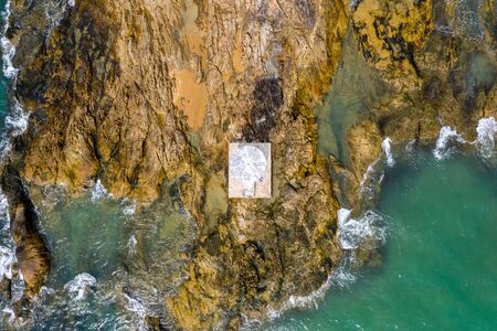 Top down aerial view of a small lighthouse on offshore rocks in a tropical ocean