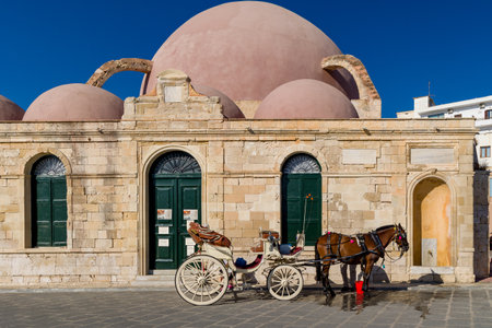 CHANIA, CRETE - 18 JULY 2021: Horses and carriageways await tourists near the ancient mosque on the seafront of Chania, Crete.のeditorial素材