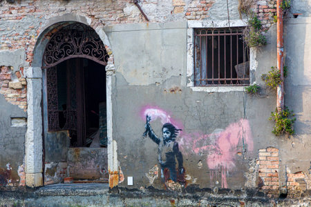VENICE, ITALY - MARCH 28 2022: Street art known as "The Migrant Child" on the side of a small building next to a canal in the back streets of Veniceのeditorial素材