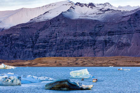 Tourist boats exploring icebergs in a glacial lagoon at dusk (Jokusarlon lagoon, Iceland)