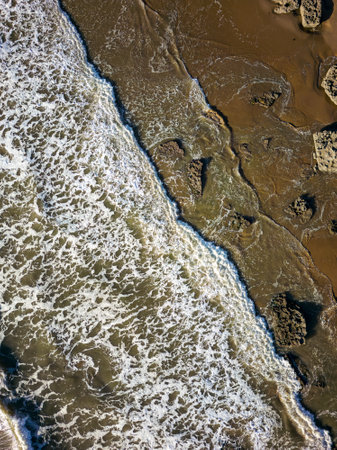 Top down areial view of waves breaking against rocks and a sandy beach.の写真素材